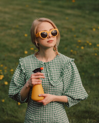 Style blonde in yellow sunglasses and green dress with spray on a meadow