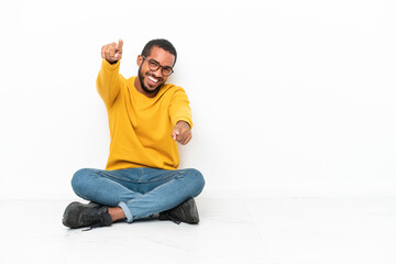 Obraz premium Young Ecuadorian man sitting on the floor isolated on white wall points finger at you while smiling