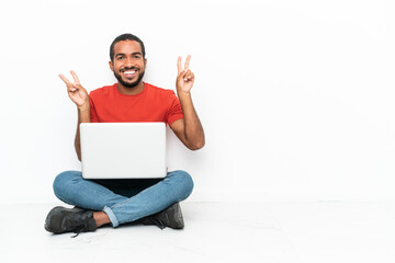 Young Ecuadorian man with a laptop sitting on the floor isolated on white background showing...