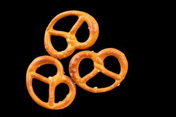 Macro photograph of three small pretzels with salt on black background