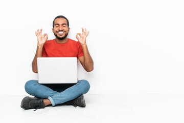 Young Ecuadorian man with a laptop sitting on the floor isolated on white background in zen pose