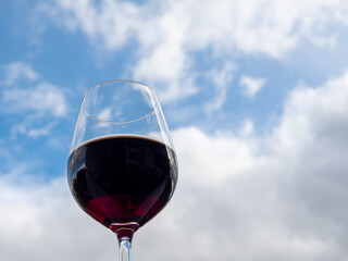 A glass of red wine against a blue sky with white clouds.
