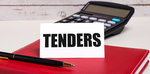 On the office desk there is a burgundy notebook, a calculator, a pen and a white card with the text TENDERS. Business concept.