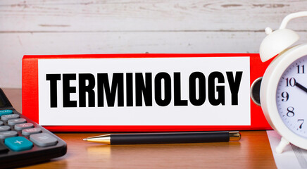 Red folder for papers with the text TERMINOLOGY, white alarm clock, calculator and pen on the...