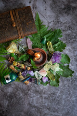 witch altar with minerals, candle, green leaves, book, magic things on dark background. wiccan...