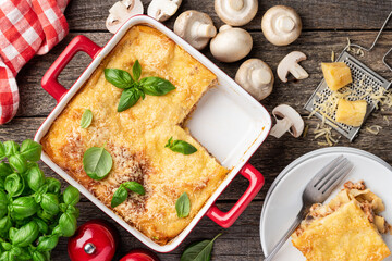 Lasagna with meat and mushrooms in a red ceramic form. Slice of lasagna on a plate. An Italian traditional dish.  Top view
