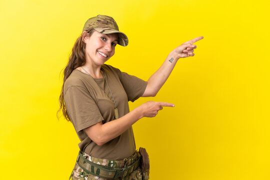 Military caucasian woman with dog tag isolated on yellow background pointing finger to the side and presenting a product