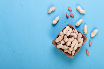 fresh peanuts in a shell in a wooden dish on a bright blue slate, concrete or stone background. lots of nuts. the concept of proper nutrition. top view.