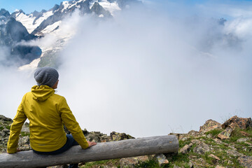 A tourist in a yellow jacket and a knitted hat on the top of high rocks. Sports and active life concept