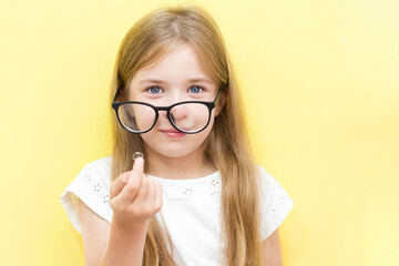A cheerful girl on a yellow background wearing glasses and holding a contact lens. The concept of...