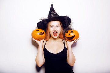 Beautiful girl witch is holding a pumpkin in her hands. Woman celebrating halloween, joy and a smile on her face