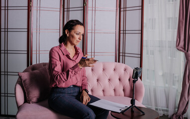 a woman in a pink shirt is sitting on the sofa and conducting an online consultation using her phone