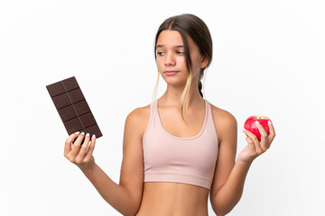 Little caucasian girl isolated on white background having doubts while taking a chocolate tablet in...