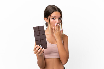 Little caucasian girl isolated on white background taking a chocolate tablet and surprised