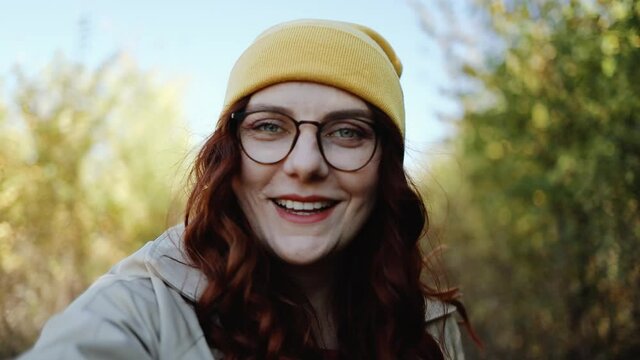 Beautiful curly-haired girl in a stylish clothes and glasses smiles and laughs at the camera, enjoying nature and walking in the autumn park