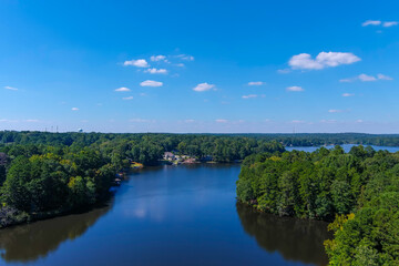 Fototapeta na wymiar a breathtaking aerial shot of the still blue waters of the lake with vast miles of lush green trees with homes and boat docks, blue sky and clouds at Lake Peachtree in Peachtree City Georgia