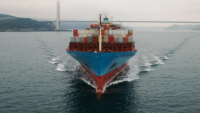 Aerial frontal view as a cargo ship ploughs through calm waters of Bosphorus. Vessel heading towards the camera. Prow and container loaded front deck of the ship underway. Bulbous bow breaking waves
