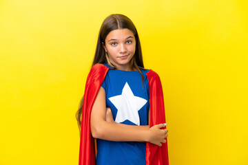 Little caucasian superhero girl isolated on yellow background making doubts gesture while lifting the shoulders