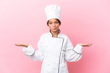 Little caucasian chef girl isolated on pink background having doubts while raising hands