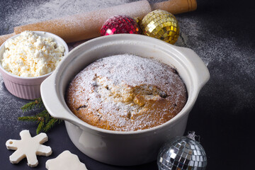 Christmas traditional curd cake with raisins and powdered sugar in a baking dish on a black background with flour front view