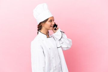 Little caucasian chef girl isolated on pink background keeping a conversation with the mobile phone