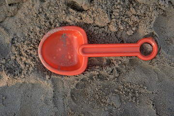 Fototapeta na wymiar Isolated red toy shovel in the wet sand. Children's beach games. Summer. Horizontal and top view