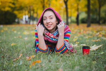Autumn portrait of a beautiful girl who lies on the grass in a city park and smiles