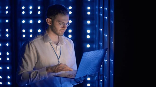 Male Server Engineer in Data Center. IT engineer inspecting a secure server cabinet using modern technology laptop coworking in data center.