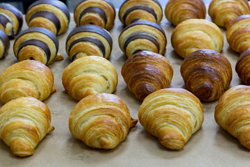 Obraz na płótnie Canvas Many croissants with different flavors are arranged in dense rows on the table. Manual production of handmade croissants and pastries
