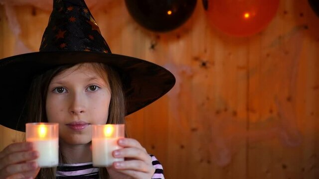 Portrait of adorable Teen Girl wearing Halloween hat holding Candles and smiling. Halloween home family party concept. Happy caucasian little kid in a witch costume celebrating Halloween at home.