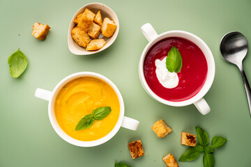 Fototapeta na wymiar Vegetarian beetroot and pumpkin cream soups in a bowls with croutons on a green background, top view