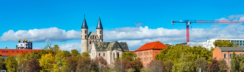 Fototapeta na wymiar Panoramic view over Church Monastery of Our Beloved in historical downtown and park of Magdeburg at blue sky with clouds and golden Autumn colors with construction crane, Magdeburg, Germany.