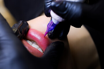 the master performs a tattoo of the lower lip stretching the lips with his fingers the model smiles...