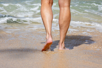 Female legs walking on sandy ocean beach