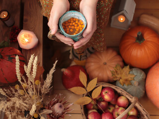 The cup of sea buckthorn tea in the woman hands with pumpkins and candles