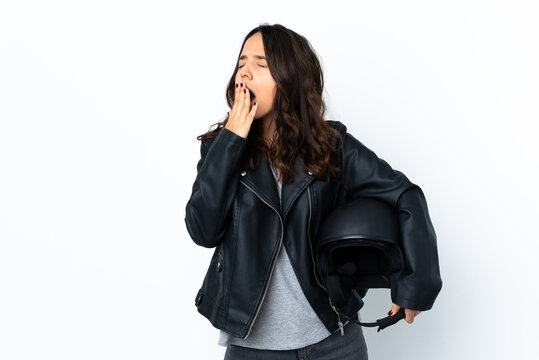 Young woman holding a motorcycle helmet over isolated white background yawning and covering wide open mouth with hand