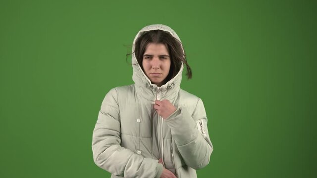 beautiful girl trying to hide from the wind and cold wearing a jacket on the green background