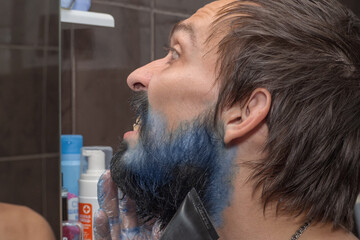 A mustachioed man with a beard is trying to dye his beard blue