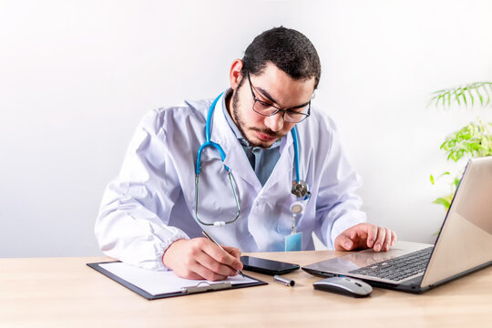 Doctor Sitting Alone At Desk In His Office Doing Paper Work.