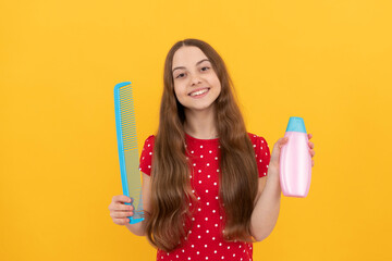 happy kid long hair showing conditioner and comb on yellow background, haircare