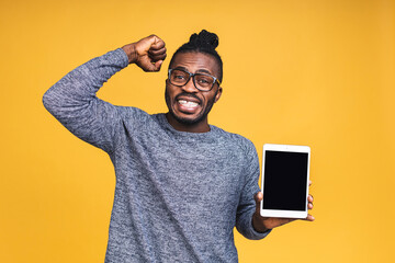 Laughing happy Young African American black man Holding a Touch Pad Tablet PC isolated over yellow Background.
