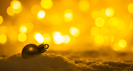 Dark silhouette of a Christmas ball in a snowdrift against a background of orange bokeh in a blur.