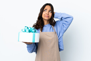 Pastry chef holding a big cake over isolated white background frustrated and covering ears