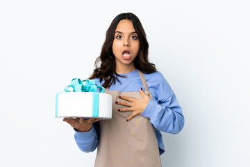 Pastry chef holding a big cake over isolated white background surprised and shocked while looking right