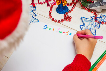 Little boy in Santa hat writes letter to Santa Claus. Kid in Santa hat writing wish list