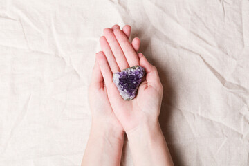 druse raw purple amethyst crystal on piece of stone on woman hand on grey linen