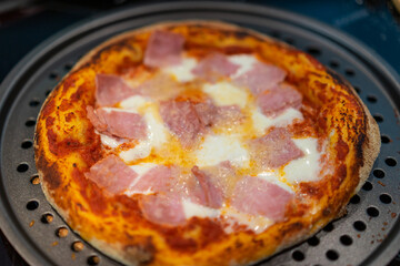Homemade oven pizza with tomato sauce, mozzarella cheese, ham and parmesan.