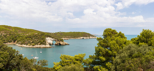 Obraz premium Arch of San Felice, Vieste. Gargano promontory with rocks in the sea, trees and vegetation, boats. Concept of vacation on the Gargano in Puglia, Italy.