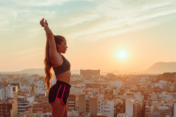 pretty young woman does yoga overlooking the city at sunset outdoors