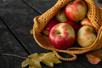 Red fresh apples in a yellow crocheted bag on a wooden table.